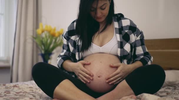 怀孕3个月 孕妇在8个月内爱抚怀孕的肚子 宝宝坐在床上轻轻地摸着肚子 — 图库视频影像