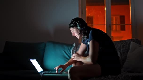 妇女夜间在客厅里使用笔记本电脑 坐在沙发上 耳机打开 — 图库视频影像