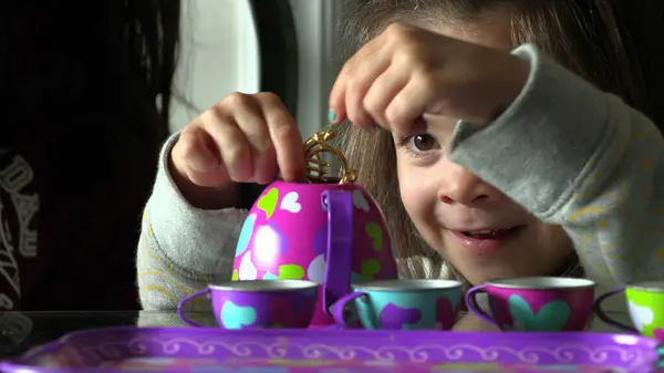 Cute little girl playing with tea cups indoors. Imaginative child plays serving tea
