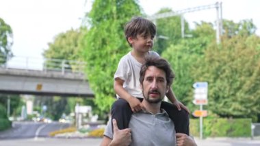 Oğul Baba 'nın Omzunda - Sırtında. Güneşli bir günde, kaldırımda kameraya bakan ebeveyn ve çocuğun portresi