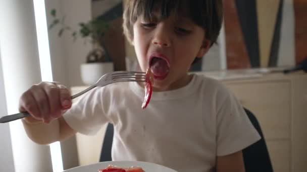 吃东西的时候把一块食物掉在孩子的腿上 笨手笨脚的小男孩吃芝士蛋糕草莓甜点弄得一团糟 — 图库视频影像