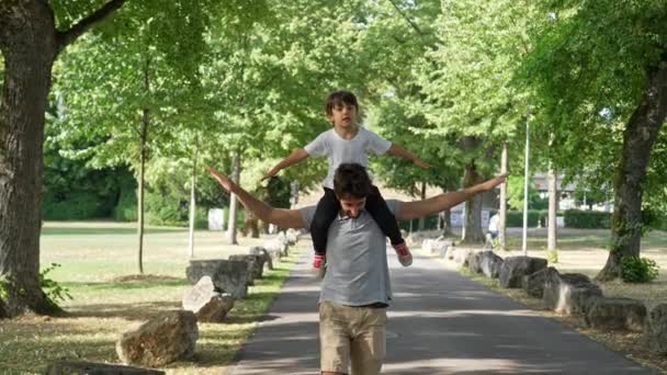 Lush Park에서 아버지는 놀이에서 비행기 제스처를위한 어깨에서 아들을 풀어줍니다 — 비디오