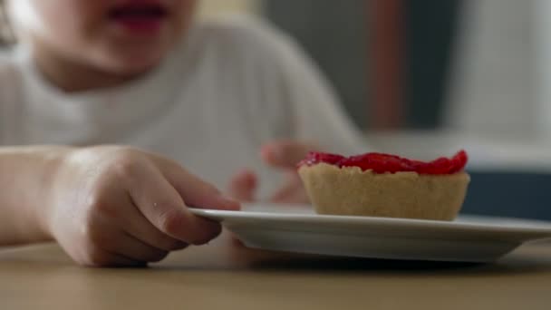 快乐的小男孩抓起甜甜的甜食盘 把芝士蛋糕滑向他 咬了一口 狼吞虎咽地吃着 孩子们的近视脸和手享受着糖的处理 — 图库视频影像
