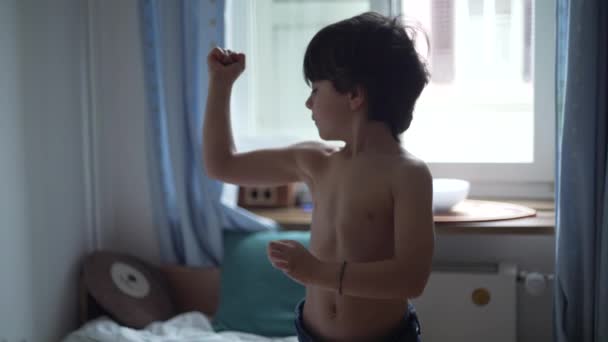 彼の筋肉を示す愛らしい小さな男の子 幸せな5歳の男性の慎重な子供は寝室で腕を柔らかく — ストック動画