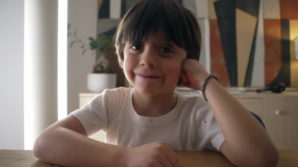 快乐英俊的小男孩靠在桌子上 看着镜头笑着 镜头前微笑的肖像特写 双手放在脸颊上 — 图库视频影像