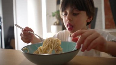 Çocuk spagetti yiyor, dağınık küçük çocuk makarnayı çatalla çeviriyor.
