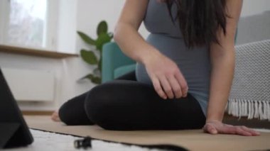 Hamile bir kadın yoga minderinde oturup günlük egzersiz rutinine hazırlanıyor. Üçüncü üç aylık hamilelik döneminde evde oturma odasında, meditasyon yapmaya hazırlanıyor.