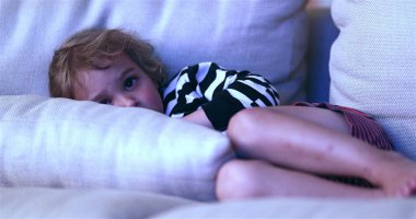 Child watching TV screen while laid in living-room sofa