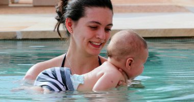 Happy mother with newborn baby son at the swimming pool water