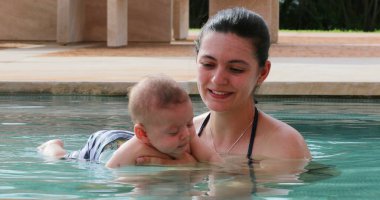 Mother and newborn baby infant son together at the swimming pool water