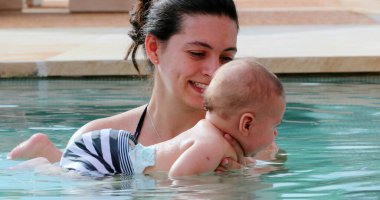 Happy mother with newborn baby son at the swimming pool water