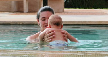 Happy mother with newborn baby son at the swimming pool water