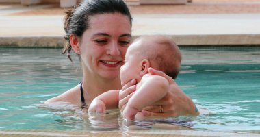 Mother holding newborn baby inside swimming pool water