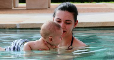 Newborn baby inside swimming pool water with mother