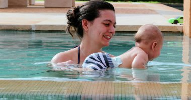 Newborn baby inside swimming pool water with mother