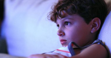 Child watching TV screen, casual candid young boy seated at living-room sofa