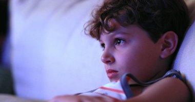 Child watching TV screen, casual candid young boy seated at living-room sofa