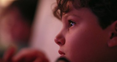 TV ekranı izleyen genç bir çocuk, ekranla hipnotize edilen samimi bir çocuk.