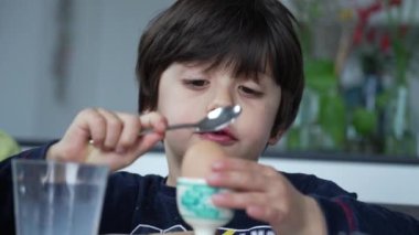 Çocuk kahvaltı masasında kaşıkla yumurta kırıyor. Küçük bir çocuk kaşıkla rafadan yumurta açıyor.