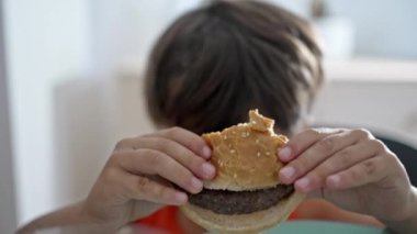 Küçük çocuk evde yaptığı hamburgerle çok mutlu ve heyecanlı.