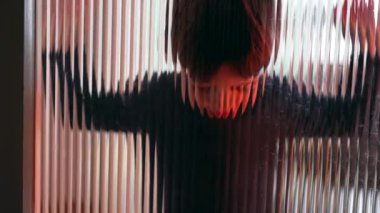 Yalnız sıkılmış çocuk cam pencereye yaslanıyor kırmızı renkli renklerle hiçbir şey yapmadan mücadele ediyor.
