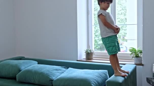 家庭中的有趣场景 小男孩爬上沙发的扶手 向后翻滚 滑向库希翁 — 图库视频影像
