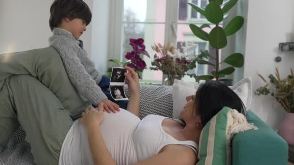 母子共享快乐温馨的时刻 在怀孕后期躺在沙发上 细看小弟弟的超声波 轻柔触摸美女 — 图库视频影像