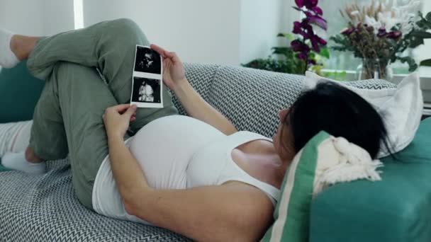 怀孕妇女躺在沙发上 看着她怀孕三个月的孩子的超声波图像 预期的父母在等她的新生儿 — 图库视频影像