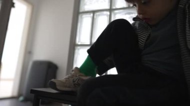 Evin kapısında ayakkabı giyen küçük bir çocuk, dışarı çıkmaya hazırlanan bir çocuk, giysiler giyen bir çocuk.