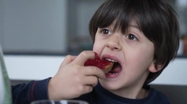 Kahvaltı masasında reçelli tost yiyen küçük bir çocuk, çocuğun yakın plan yüzü bir lokma yiyecek.