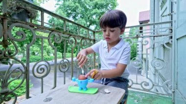 Küçük çocuk, uygun boyuttaki masasında haşlanmış yumurta ve apartmanın balkonundaki tabureden hoşlanır.