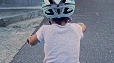 Bisiklet kaskı takan çocuk kaldırımda pedal çevirmeye başlıyor.