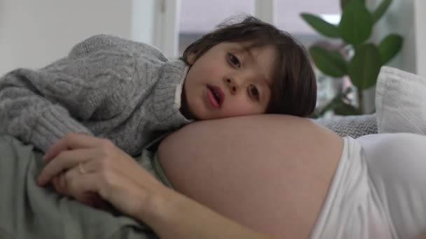 怀孕的母亲和儿子共享一个瞬间 宝宝依偎在床上 倾听宝宝的移动 在安静舒适的家中躺在沙发上的真实的结合场景 — 图库视频影像