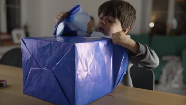 子供はプレゼントを包むことなく 1人の小さな男の子は熱心に箱を開けたいパッケージから紙を引き裂きます — ストック動画
