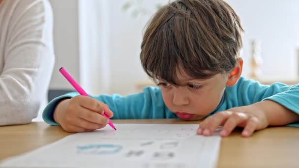 小さな男の子はペンでイラストの周りに手紙を書くことを学びます — ストック動画