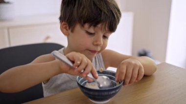 Küçük çocuk mısır gevreğini kaseden çıkarıp süte tıkıştırıyor.