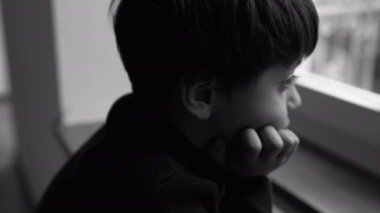 Depresyondaki çocuk melankolik bir ifadeyle pencerede duruyor ve el ele tutuşup yalnızlık ve yalnızlık hissediyor. Çocuk üzüntüsünü dramatik, siyah ve beyaz renklerle ifade ediyor.