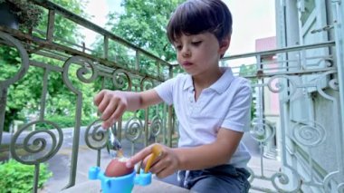 Ufaklık, balkonda kaynamış yumurta menüsünün tadını çıkarıyor, çocuk boyunda bir masada ve bankta oturuyor.