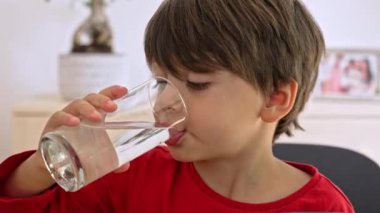 Masadaki küçük çocuk bardaktan su içiyor, yemek sırasında susamış.