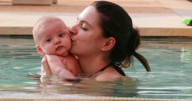 Mother kissing baby inside pool water