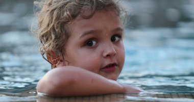 Portrait of little boy inside swimming pool water looking to camera