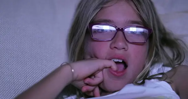 Little girl child watching TV screen in the dark wearing glasses