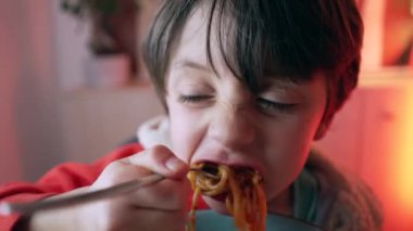Akşam yemeğinde makarnanın tadını çıkaran küçük bir çocuk, spagetti yiyen 5 yaşındaki çocuğun yakın plan yüzü.