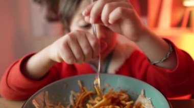 Spagetti yiyen küçük bir çocuğun portresi, 5 yaşındaki çocuğun neşeli yemek saati, makarnalı çatal çevirmede ustalaşması.