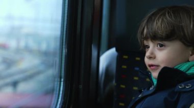 Tren penceresinden geçen manzaraya bakan küçük bir çocuk. Sonbahar sezonu seyahati sırasında atkı ve ceket giyen çocuk.