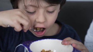 Küçük çocuk kasenin içinde kaşıkla mısır gevreği yiyor. Aç çocuk kahvaltıda buğday yiyor.