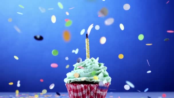 庆祝纸杯蛋糕周年 顶部点着蜡烛 五彩纸屑飘落在超级慢动作和蓝色背景下 — 图库视频影像