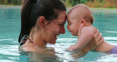 Mother and baby interaction at the swimming pool water showing love and affection smiling