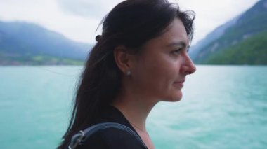 Huzurlu bir kadın tekneyle seyahat ediyor. Dağ ve göl manzarasına bakıyor. Profili yakından izliyor.