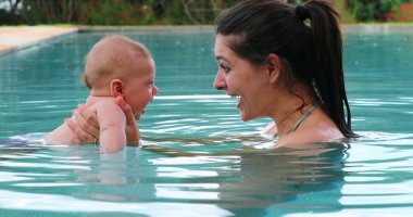 Mother holding baby son inside swimming pool water interaction